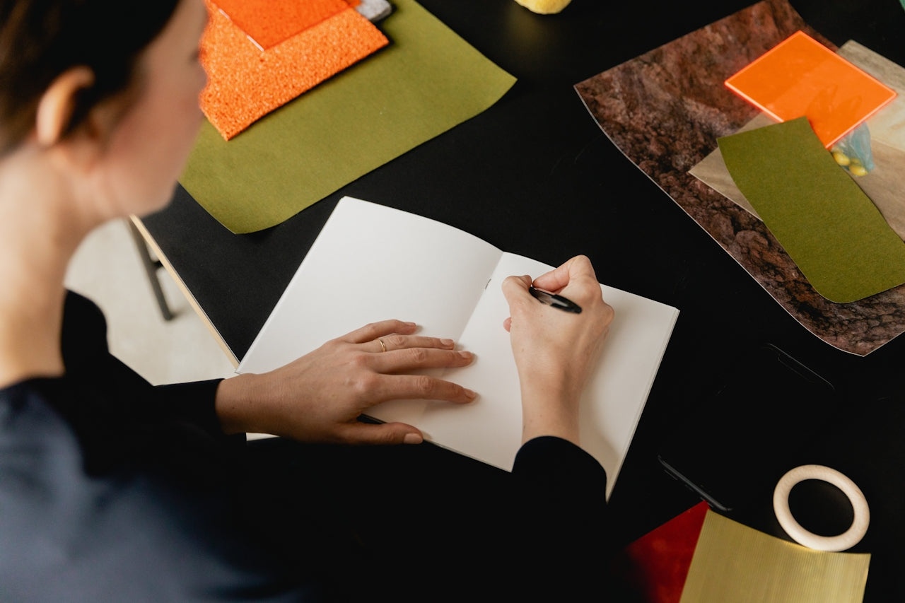 Person writing in notebook surrounded by creative materials, flow state and focused creative work with yerba maté